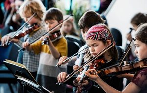 A group of children play violins together, focusing intently on their music.