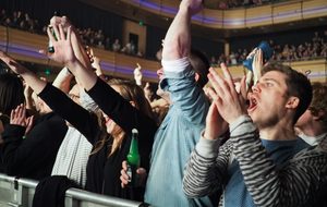 A crowd of people at a concert in Sage One cheer enthusiastically, raising their arms and clapping.