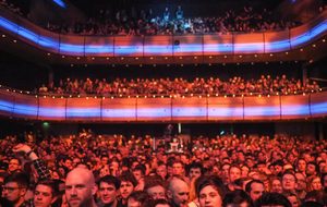 A large crowd of people stands closely packed in Sage One, facing the stage.