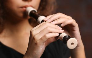 Young woman playing on recorder over brick wall background