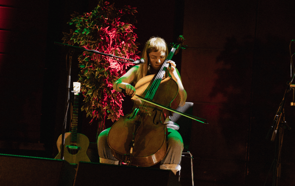 A female musician with cello under red light on stage.
