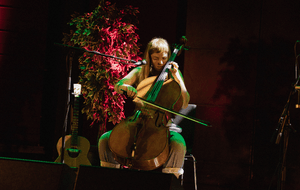 A female musician with cello under red light on stage.