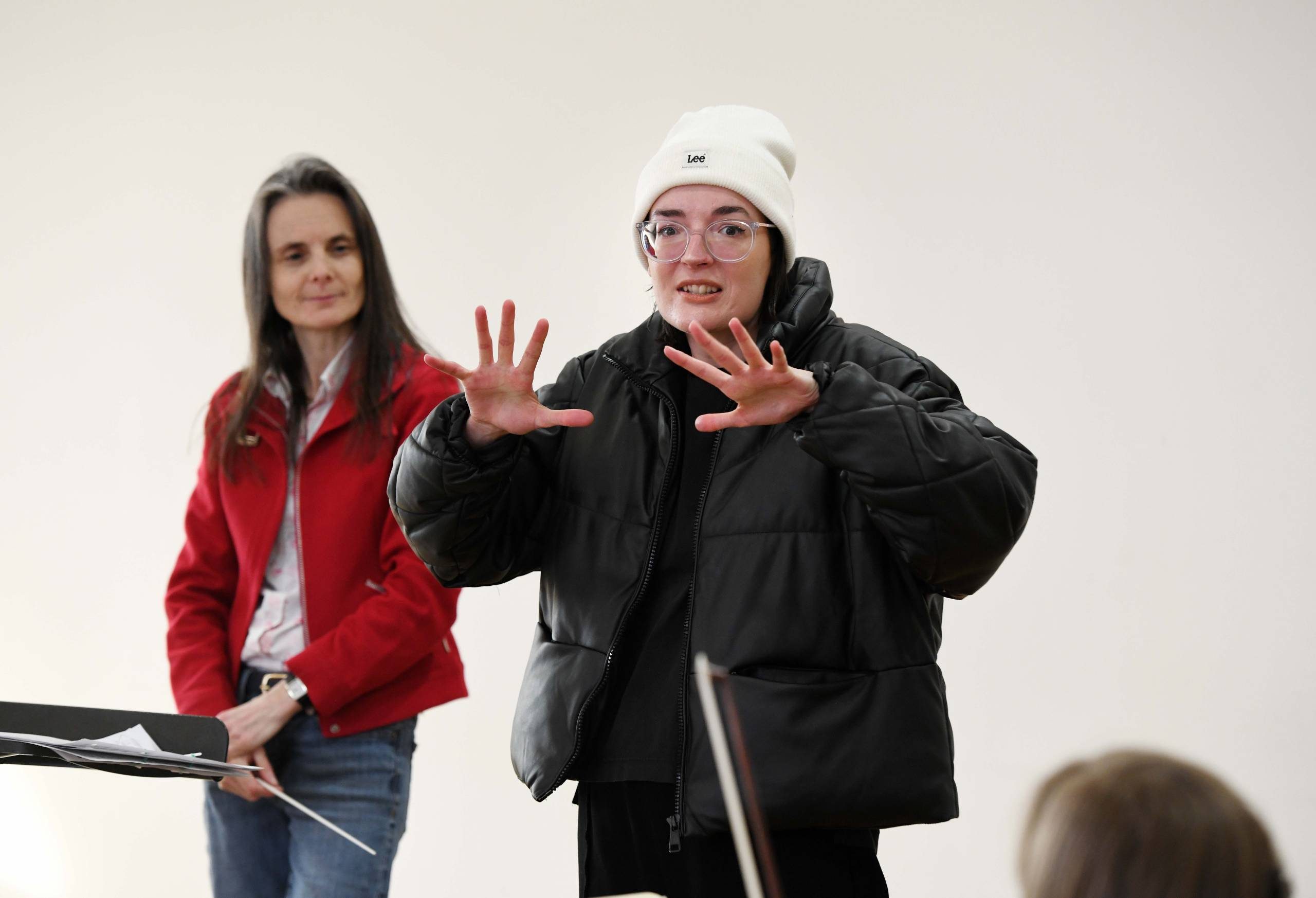 a person in a black coat and white hat with her hands up next to a woman with long hair in a red jacket