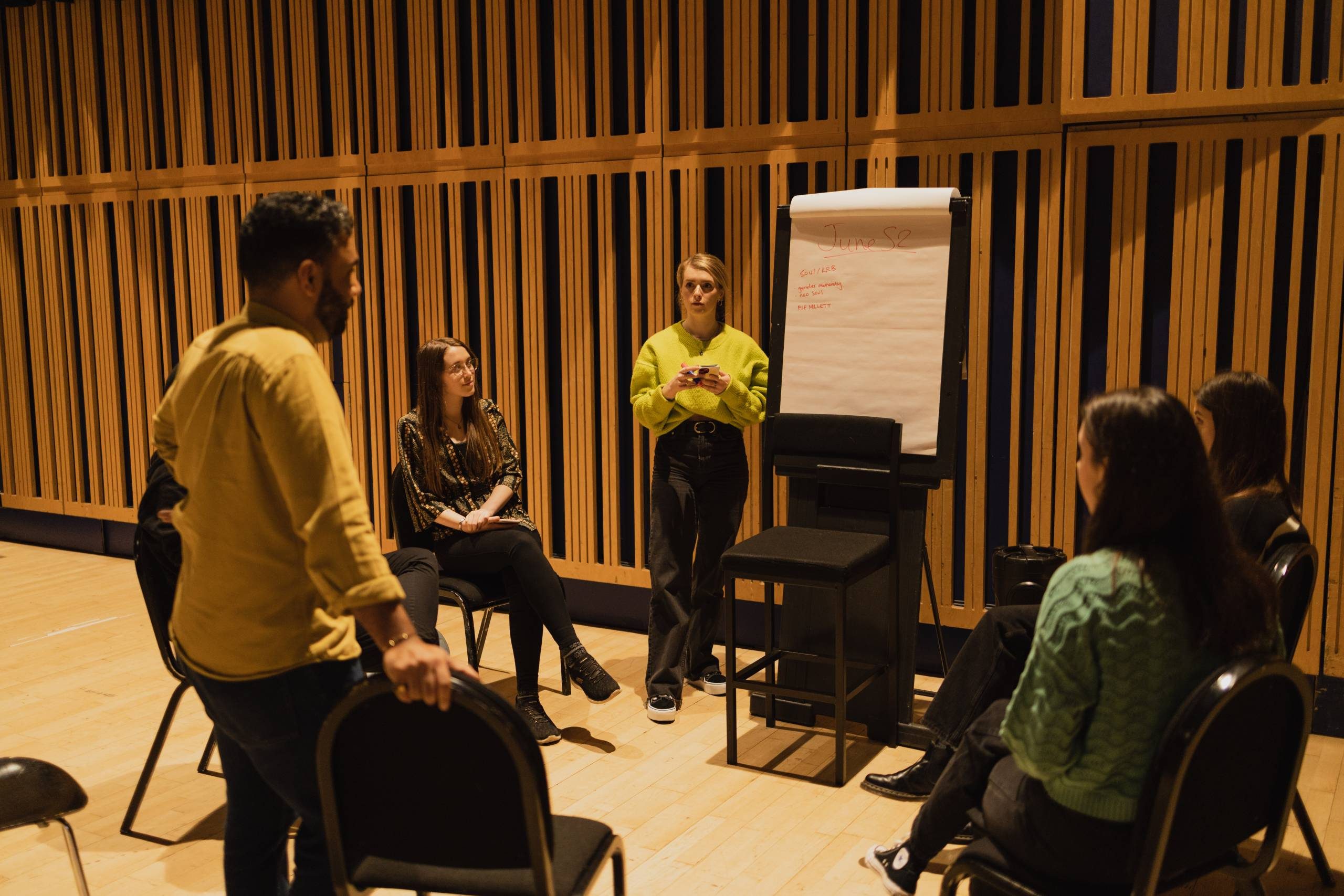 a group sitting in a circle around a white flip chart
