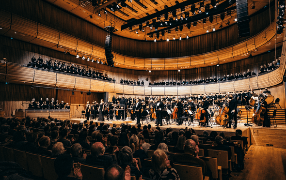 an audience clapping in a concert hall with an orchestra and choir