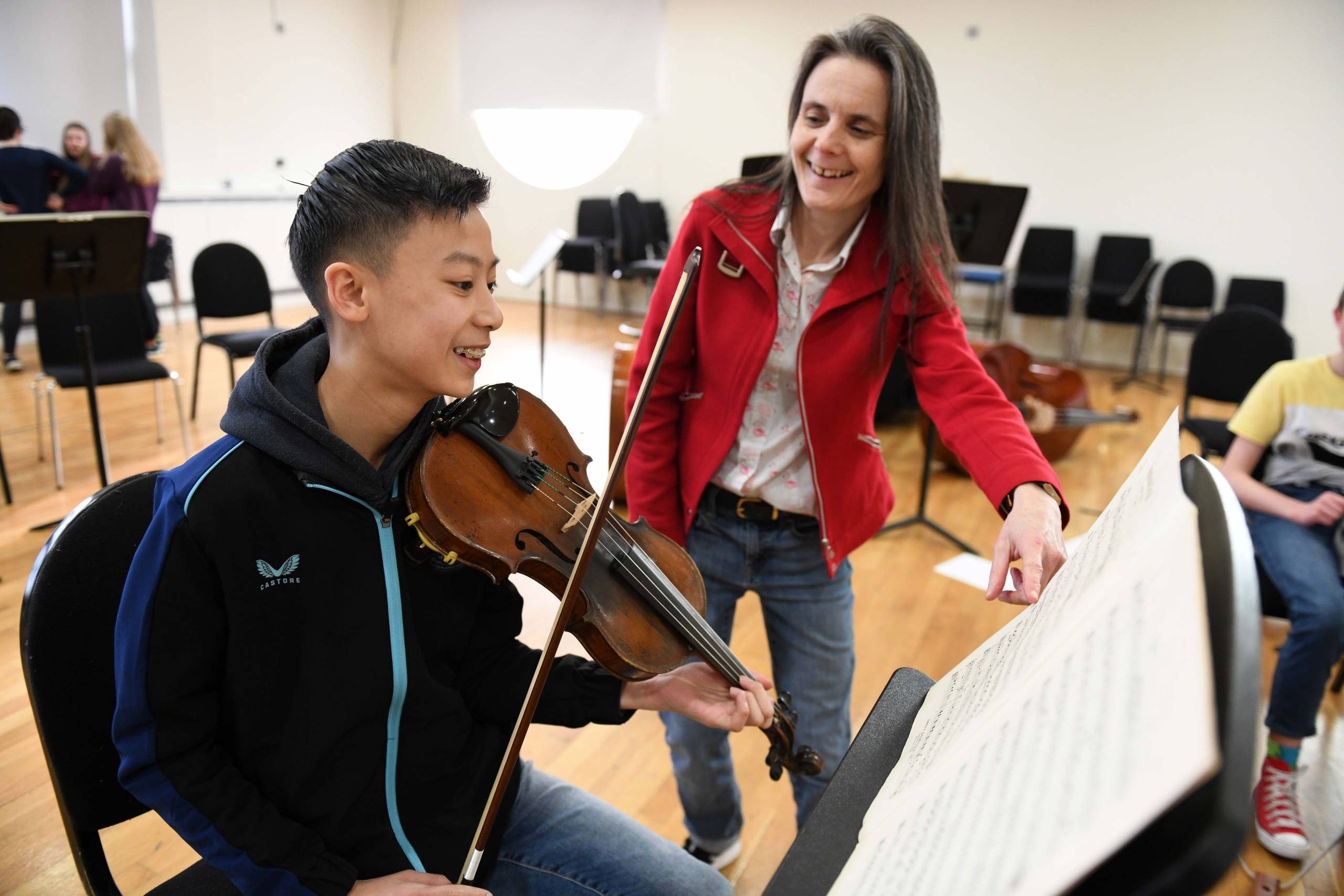 conductor in a red jacket with a young musician in a blue coat and brown violin