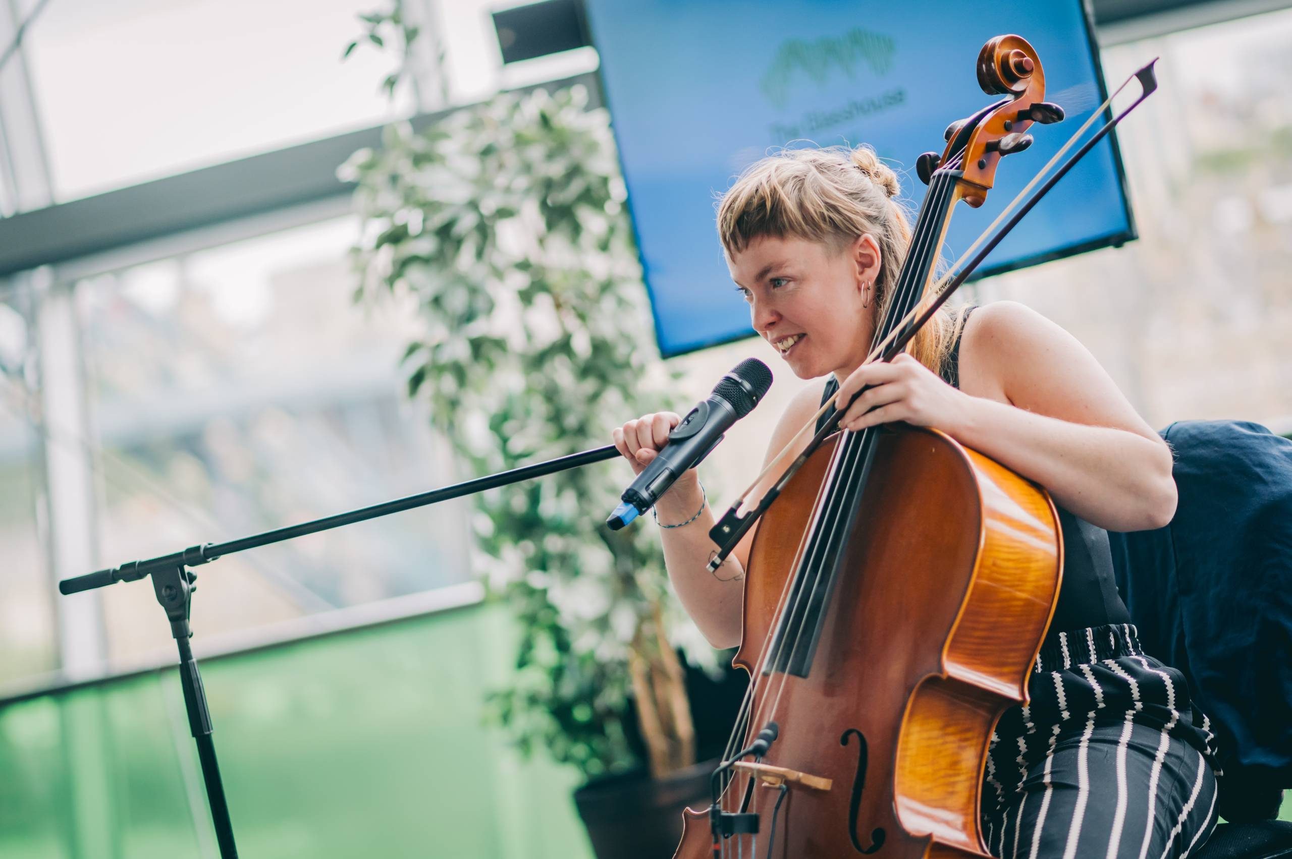 person with a brown cello and mic in their hand wearing striped trousers