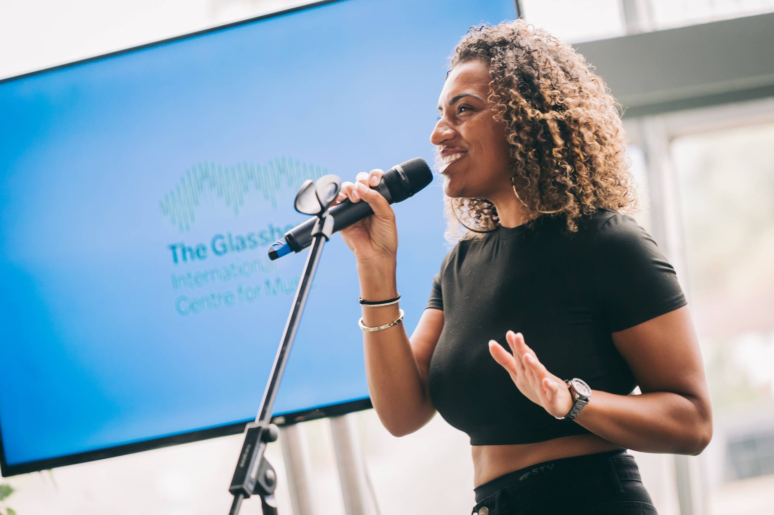 person with curly hair in front of a blue sign singing