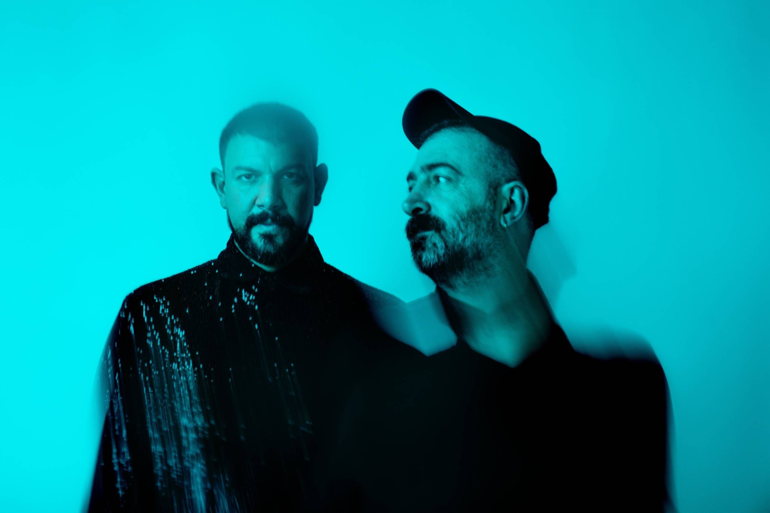 Stylised promo shot of Boys' Shorts; a head-and-shoulders photo of two men in dark clothing, one of them wearing a baseball cap and looking across and in front of the other.