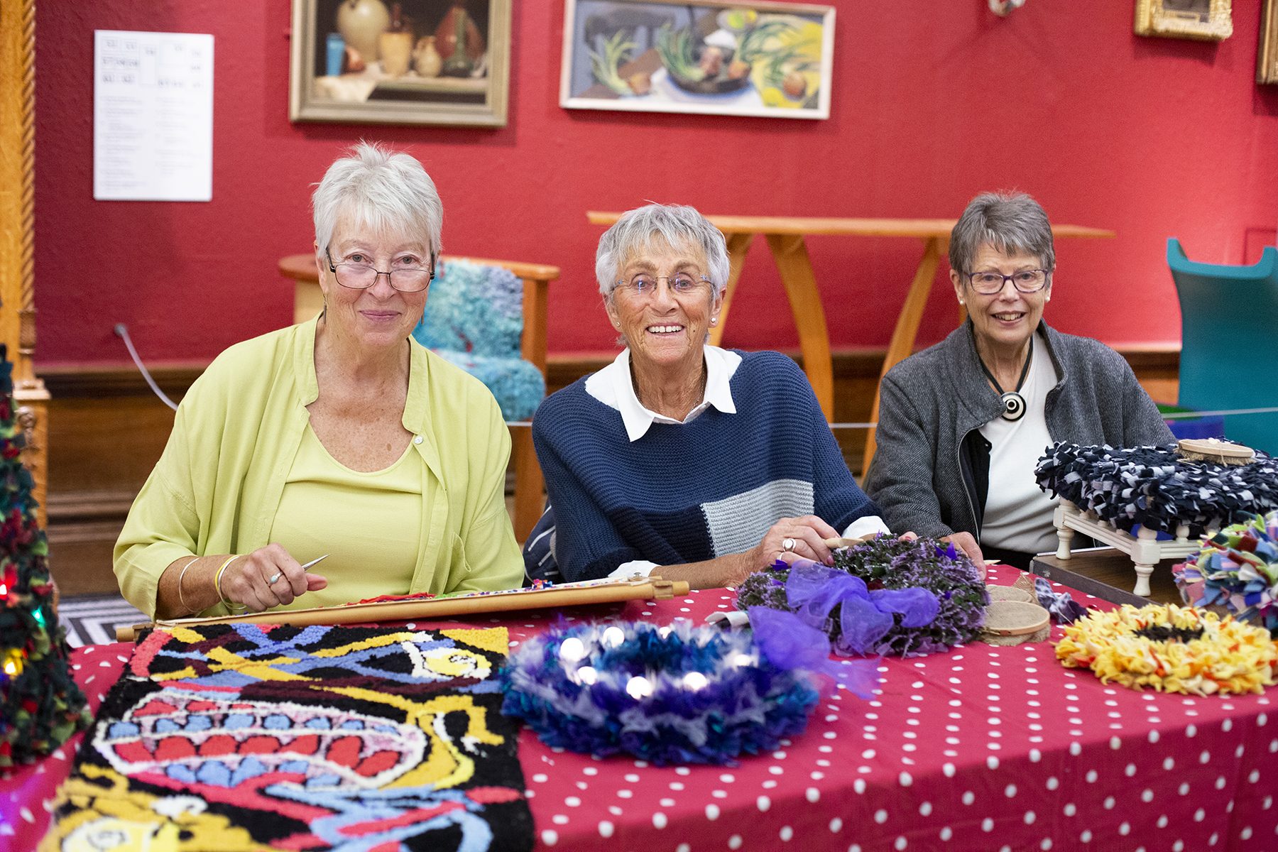 three people sitting at a red table with craft