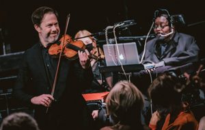 Man in black outfit with a violin and man with computerised instrument behind