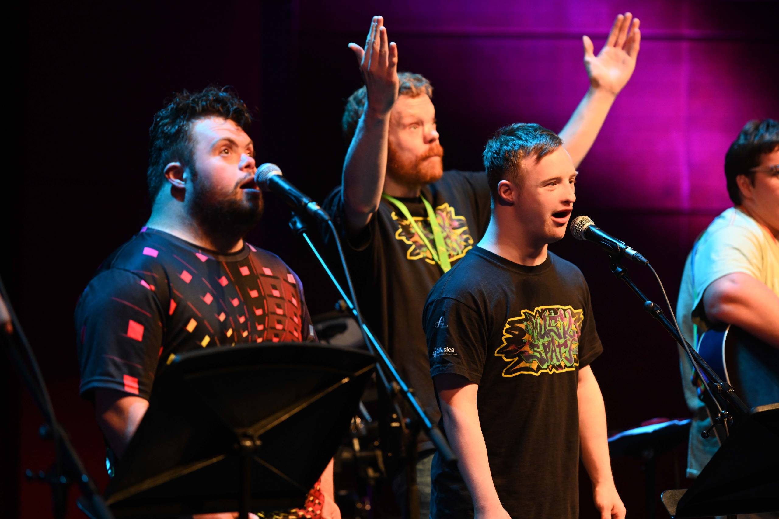 three people in black t shirts. the middle person has their hands in the air