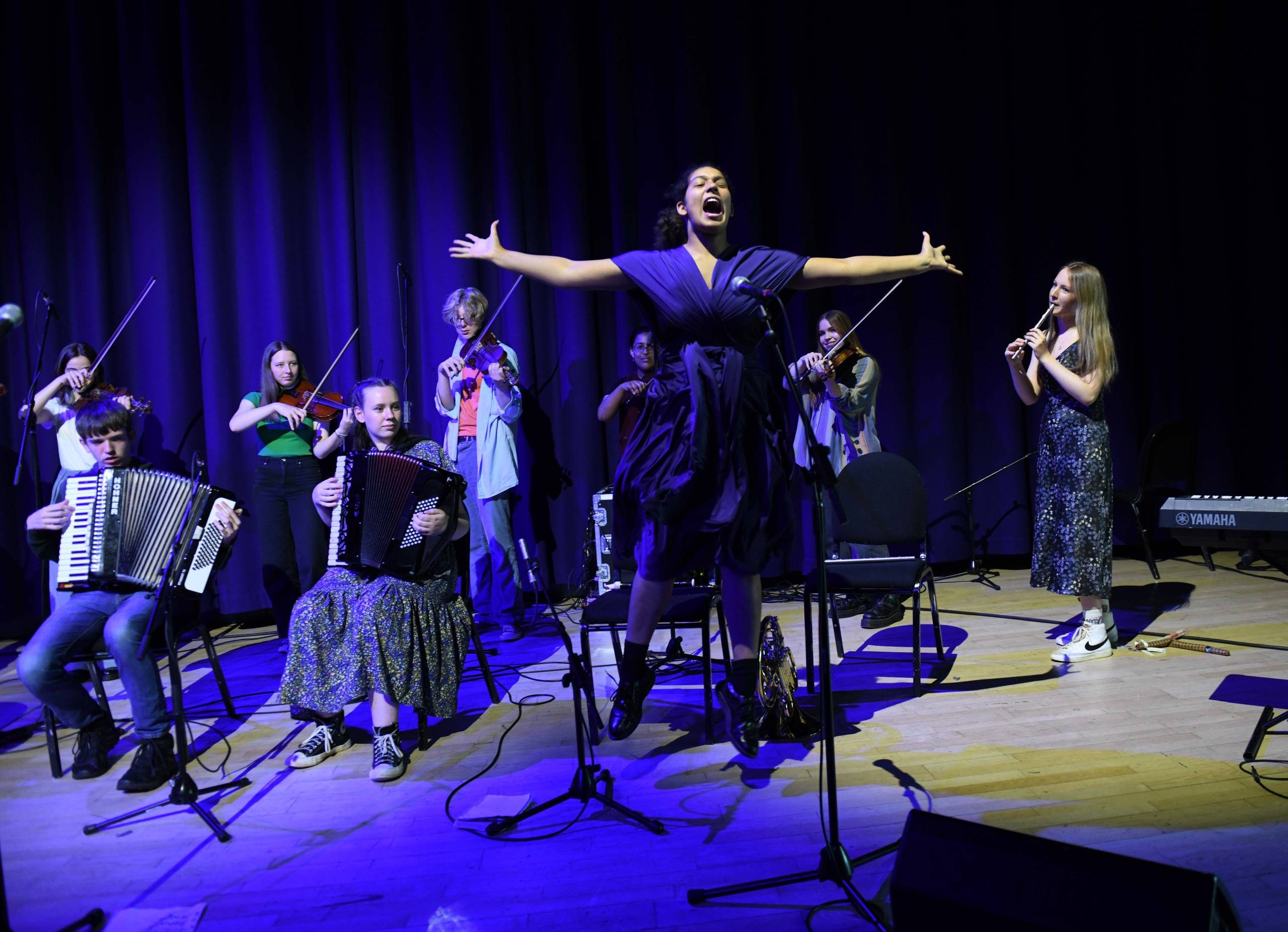 person in blue dress under blue lights jumping in the air in front of a crowd