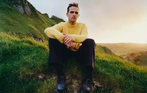 person in a yellow jumper sitting on a green hill.