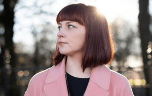 Person with brown bob and pink coat in from of trees