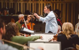 person in blue shirt and black hair conducting an orchestra
