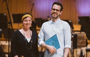 A man in a blue shirt with a book in his hands and a woman in a black top and yellow headband