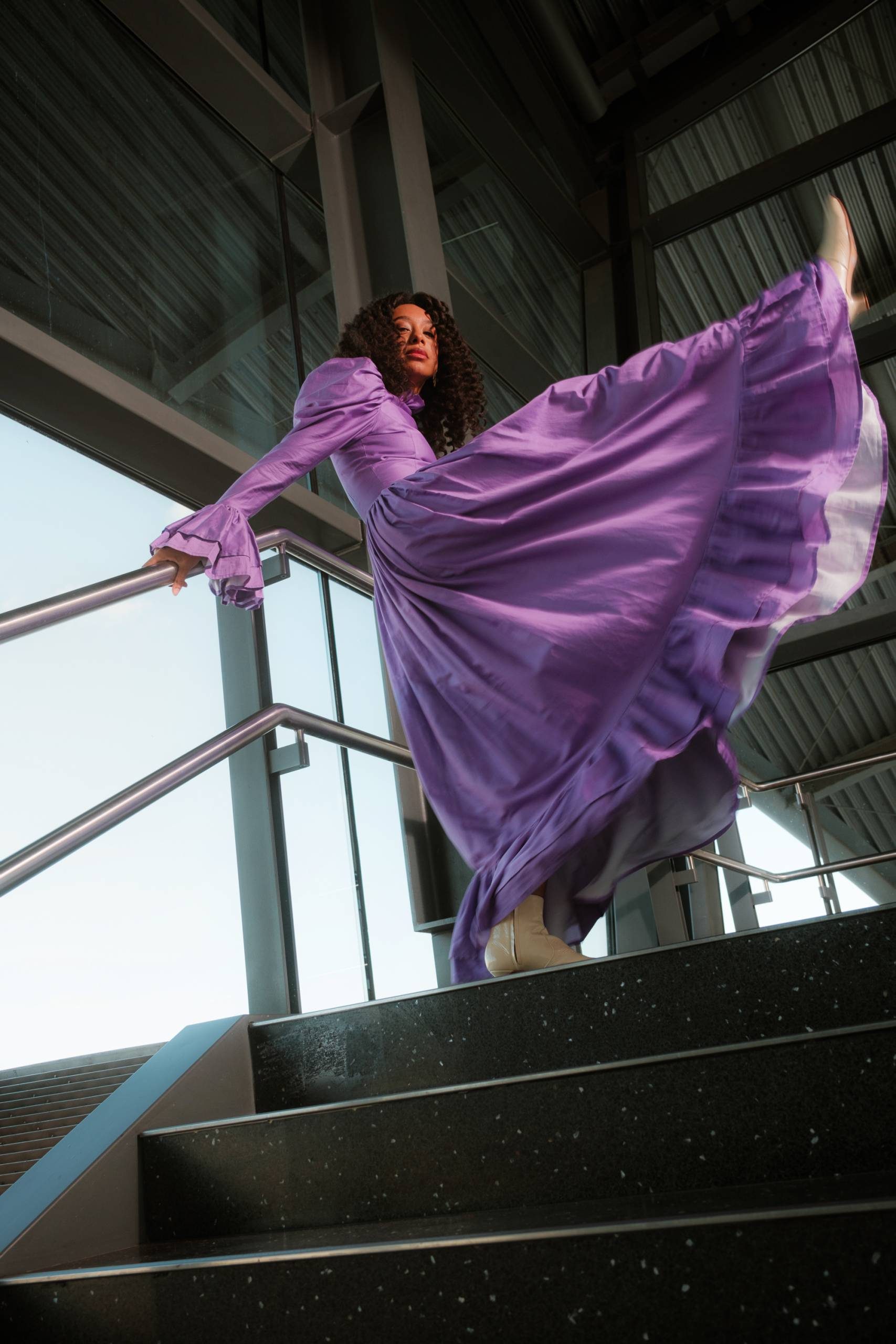 Corinne Bailey Rae standing at the top of some staors kicking one leg in the air