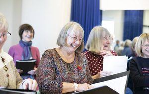 A woman with grey hair singing from a book.