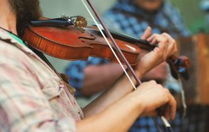 A close up of a person playing a fiddle, wearing a pale pink checked shirt.