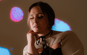 NØELLE in a cream jumper standing in front of a dotty wall.