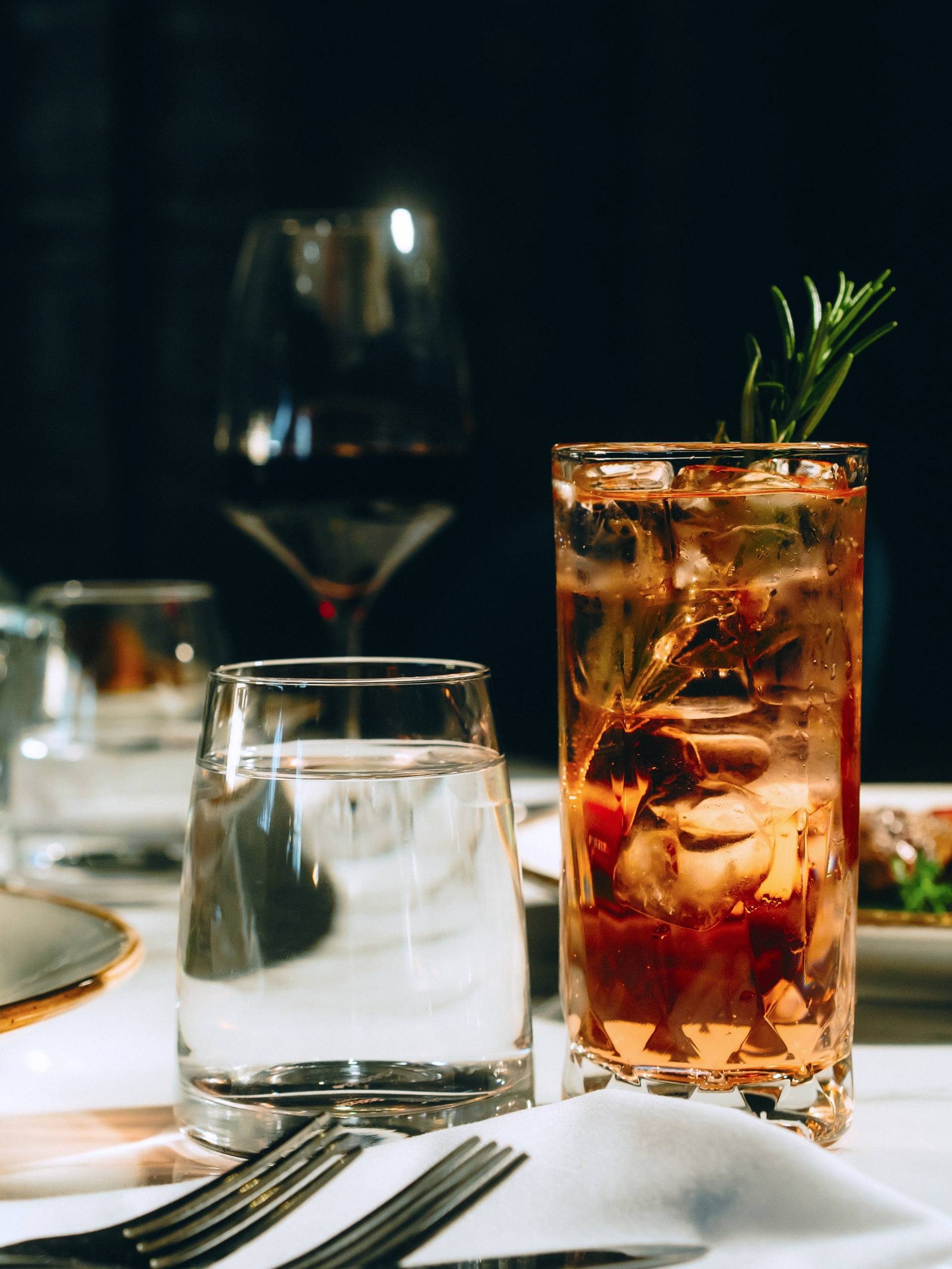 Two glasses of cocktails on a table with a white tablecloth in a darkly lit restaurant.