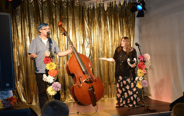 A man with blue hair and a double bass and a woman in a floral skirt.
