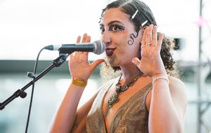 Rivkala with her hands by her head and wearing a gold dress