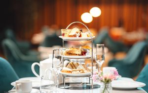 An afternoon tea rack filled with sandwiches and cakes, with a pot of tea on a table in a restaurant.