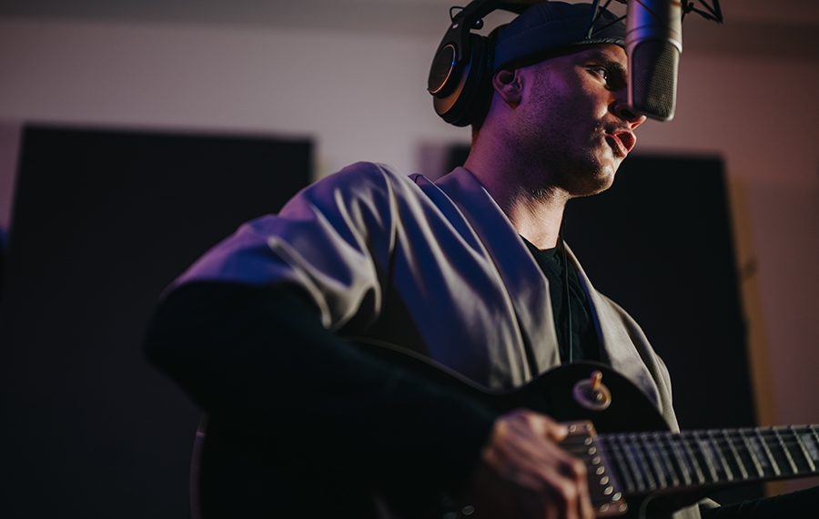 A focused musician in a recording studio plays electric guitar and sings into a microphone. The setting highlights the artist's creativity and passion for music production and performance.