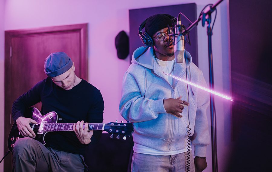 Two musicians collaborate in a professional recording studio, using a guitar and microphone. The creative atmosphere is captured with vibrant lighting, emphasizing the teamwork and passion for music.