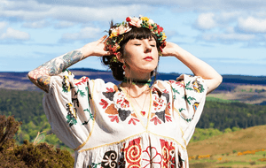 Shannon Pearl in a colourful outfit and flower crown standing on a field.