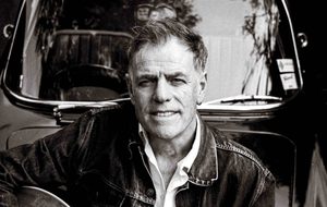 Black and white photo of Martyn Joseph, a man with short hair smile. He is wearing a denim jacket and a white shirt.
