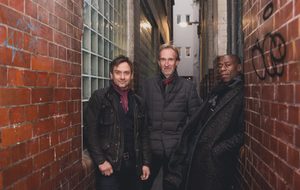 Mike + The Mechanics standing together in a narrow brick alleyway.