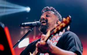 A bearded man sings into a microphone while playing the guitar.