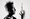 Black-and-white portrait of a spiky-haired man looking towards at a small floating violin above his raised hand with his eyes closed